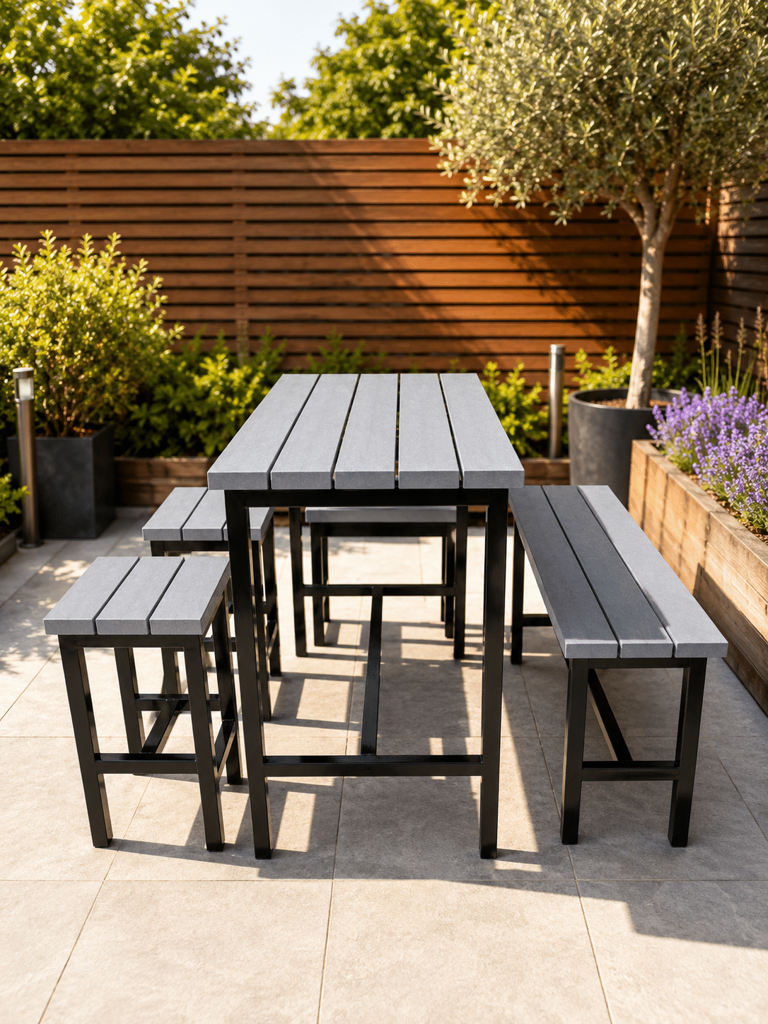 Outdoor metal dining set with a gray slatted table and matching benches on a paved patio with greenery nearby.